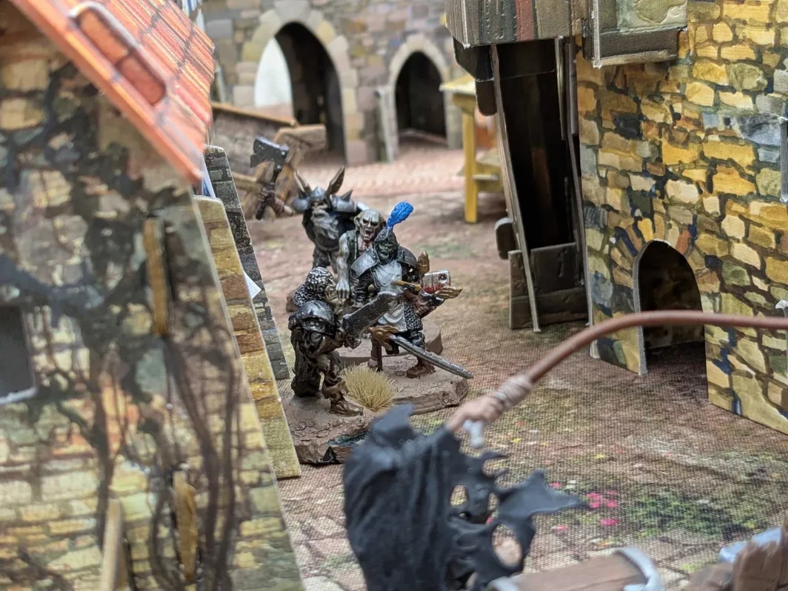 Groep ork miniaturen met bijlen en zwaarden in een steegje tussen stenen huizen op een Mordheim speeltafel