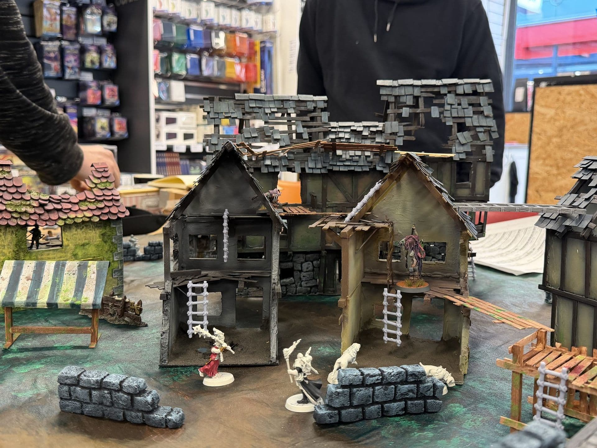 Mordheim tafel met vervallen vakwerkhuizen, ladders, een marktkraam en miniaturen tijdens de speeldag