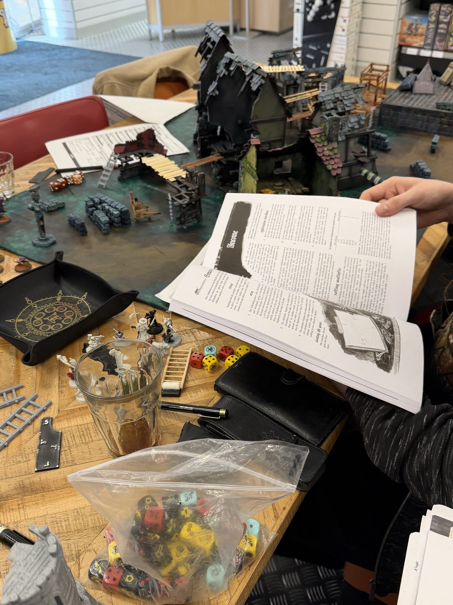Speler leest een regelboek aan tafel, met dobbelstenen, miniaturen en de speltafel ernaast