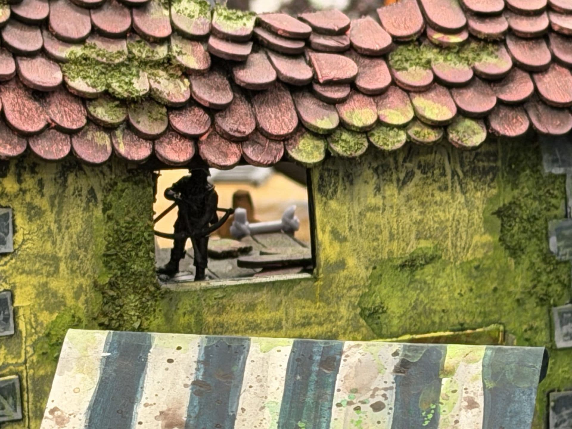 Miniatuur in een venster onder een rood pannendak met mos, boven een houten loopbrug