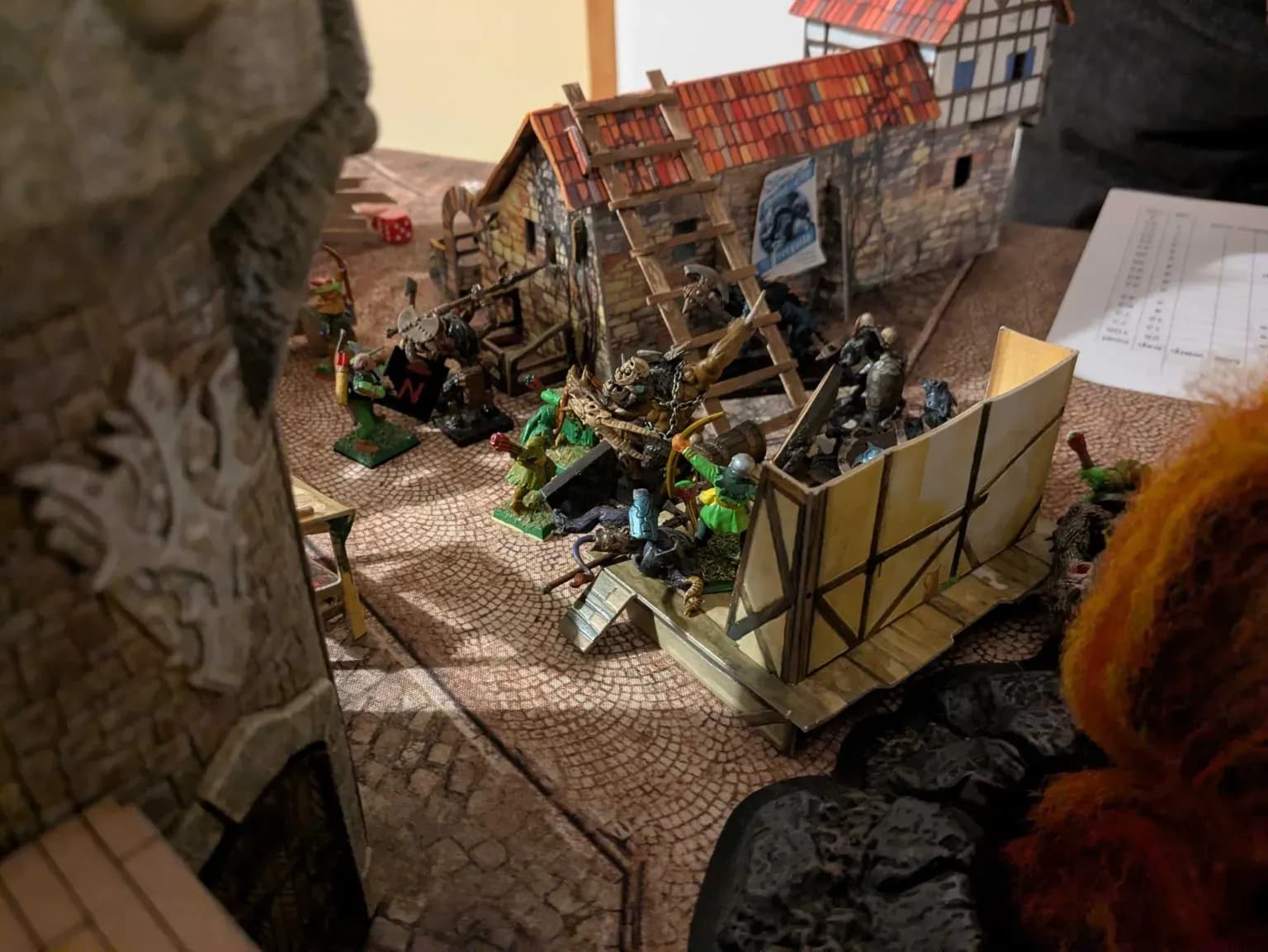 Gevecht tussen Mordheim warbands op een geplaveid plein naast een huis met een ladder