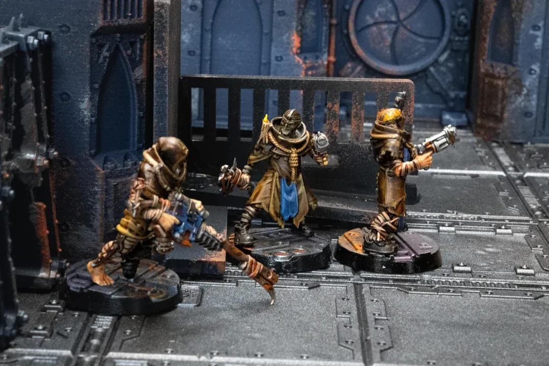 Drie Necromunda gangers in gewaden met pistolen op een industriële speeltafel